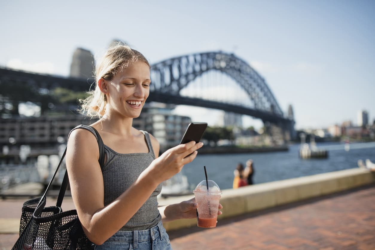 Young woman using her mobile phone in front of the Sydney Harbour Bridge in Australia