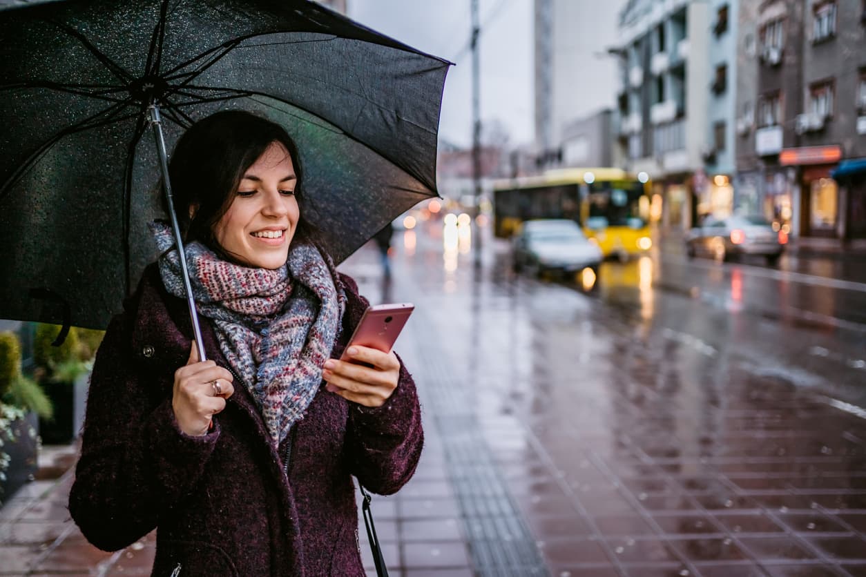 Young woman using her mobile phone in the rain